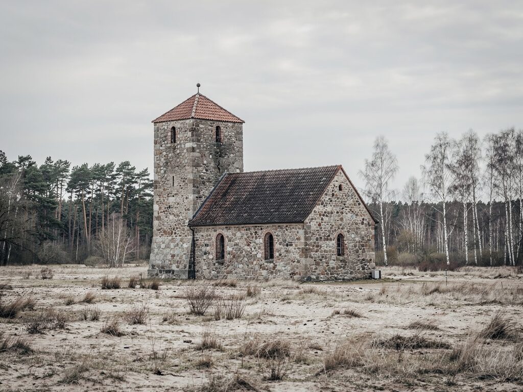 Märkische Feldsteinkirche mit quadratischem Wehrturm in der Heidelandschaft