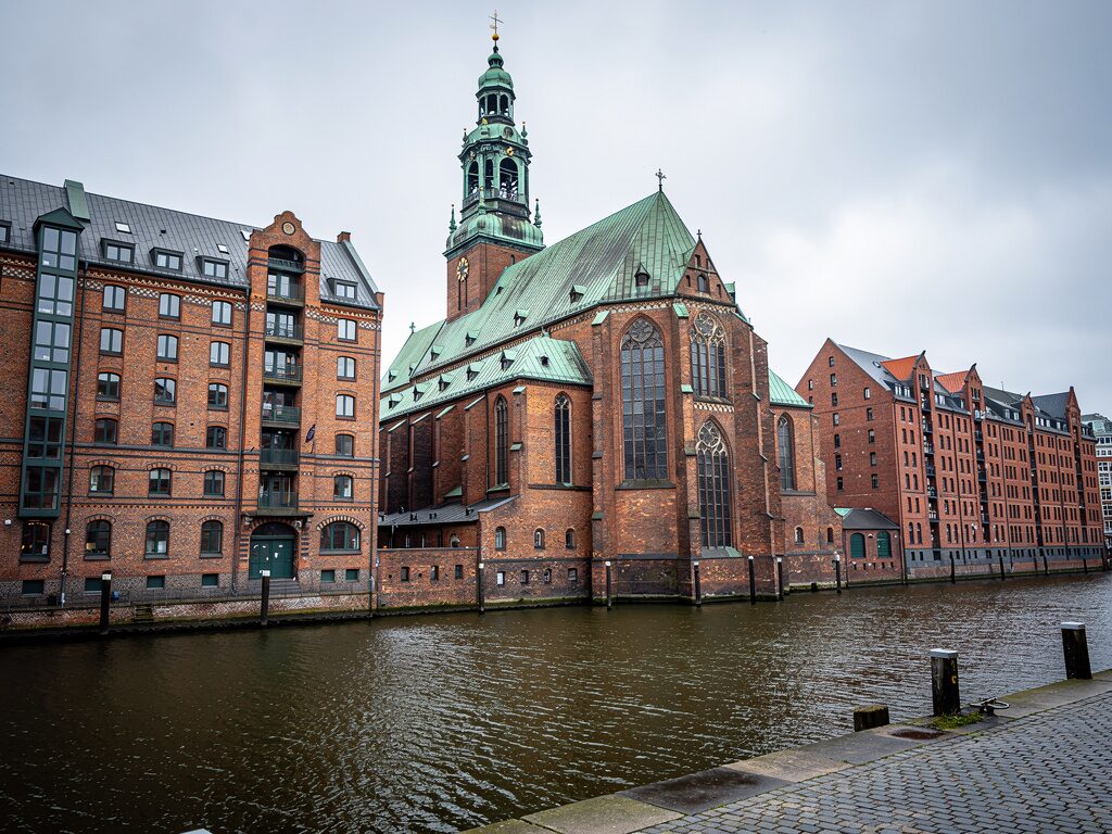 Hamburger Hauptkirche mit kupfergrünem Turm an einem Speicherstadt-Kanal