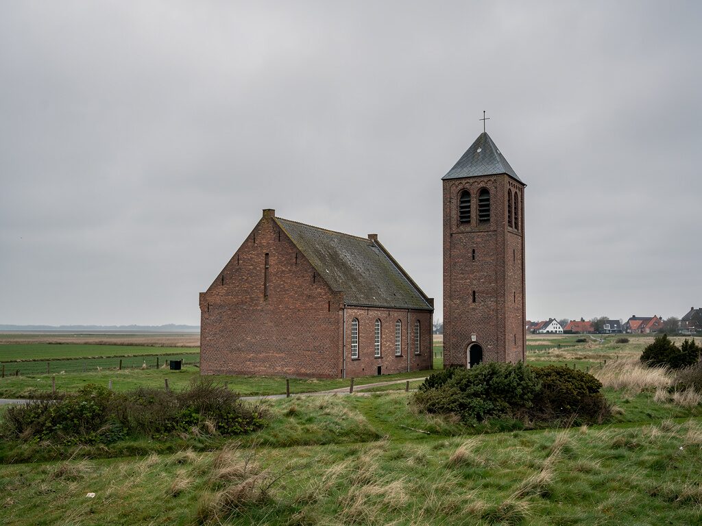 Schlichte reformierte Backsteinkirche mit freistehendem Glockenturm im ostfriesischen Marschland
