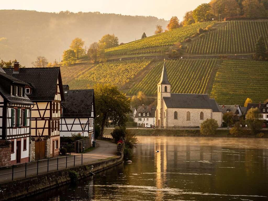 Kirche in einem Moselweindorf mit terrassierten Weinbergen im Herbstlicht