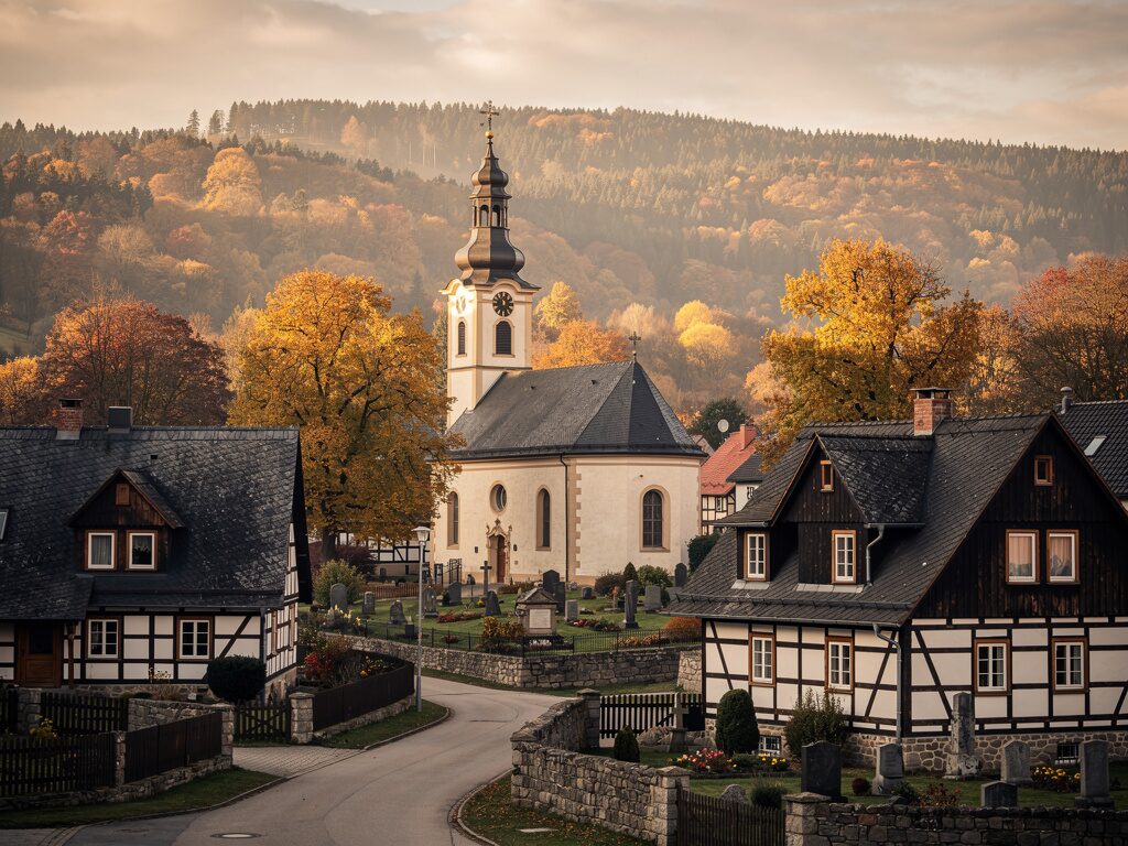 Erzgebirgische Dorfkirche mit Barockturm zwischen Umgebindehäusern im Herbst