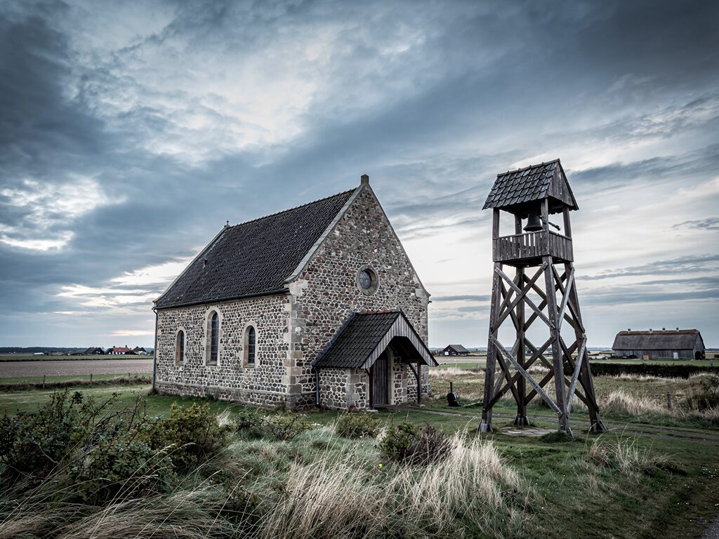 Norddeutsche Feldsteinkirche mit freistehendem Holz-Glockenturm in flacher Küstenlandschaft